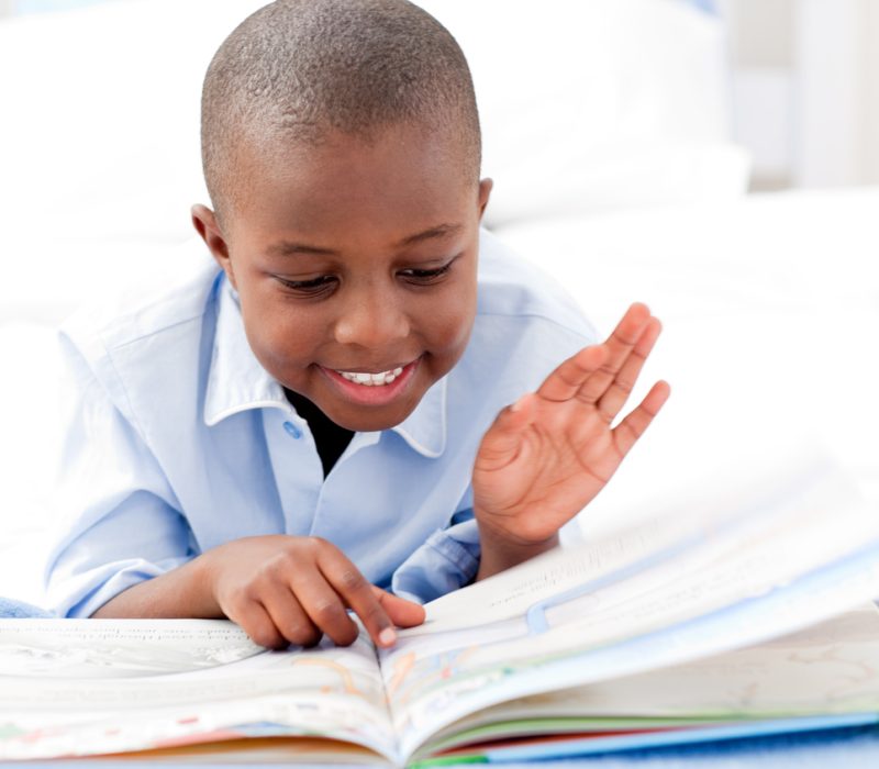 Small boy reading a book on his bed