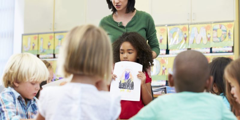 Elementary Pupil Showing Drawing To Classmates In Classroom