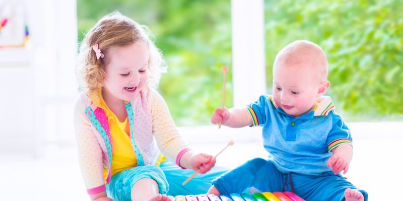 Two little children - cute curly toddler girl and a funny baby boy, brother and sister playing music, having fun with colorful xylophone at a window; kids early development class